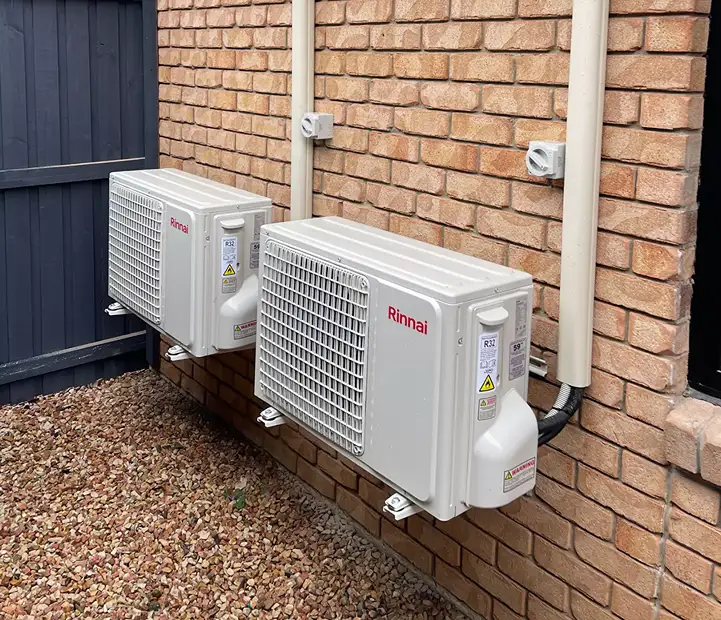 Two outdoor air conditioning units mounted on a brick wall, dual system installation.
