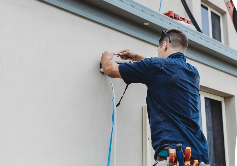 Electrician fixing exterior cabling to a wall, installation work.
