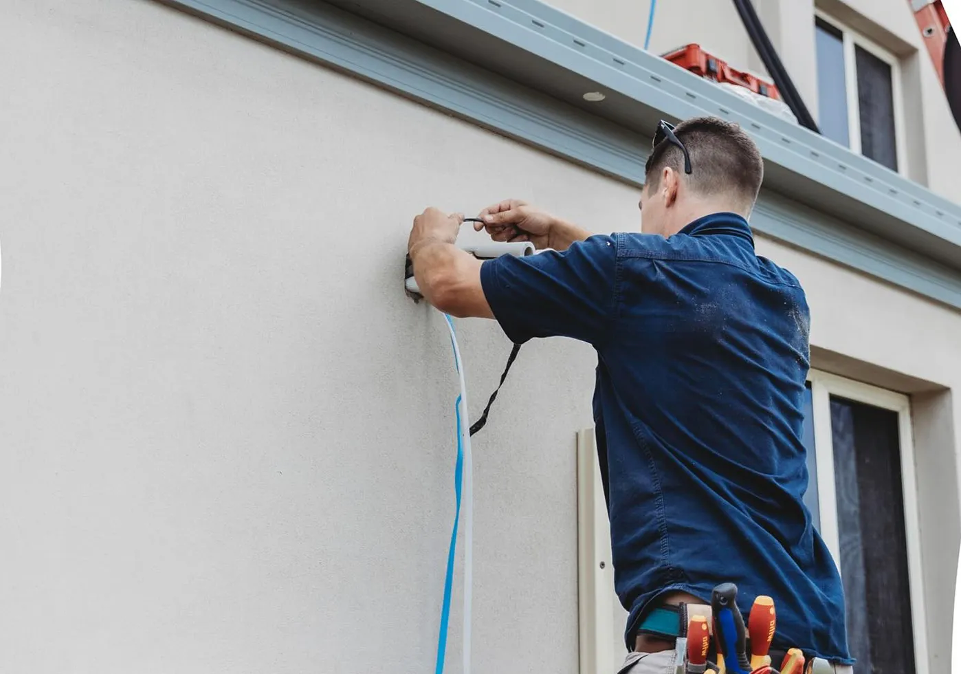 Electrician fixing exterior cabling to a wall, installation work.