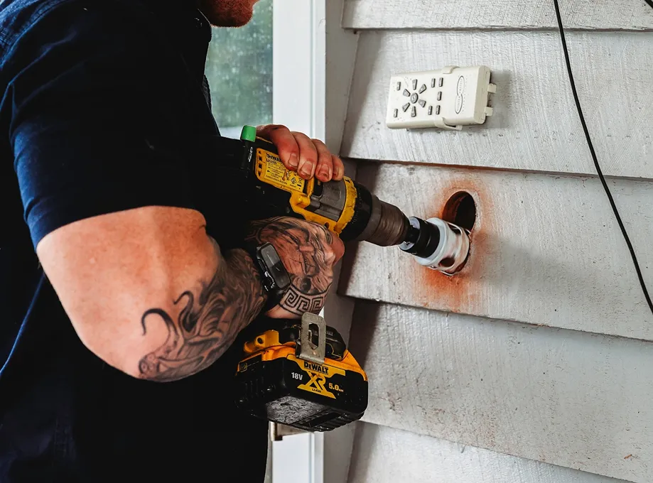 Electrician drilling into an exterior wall for fitting installation, exterior wall fitting.