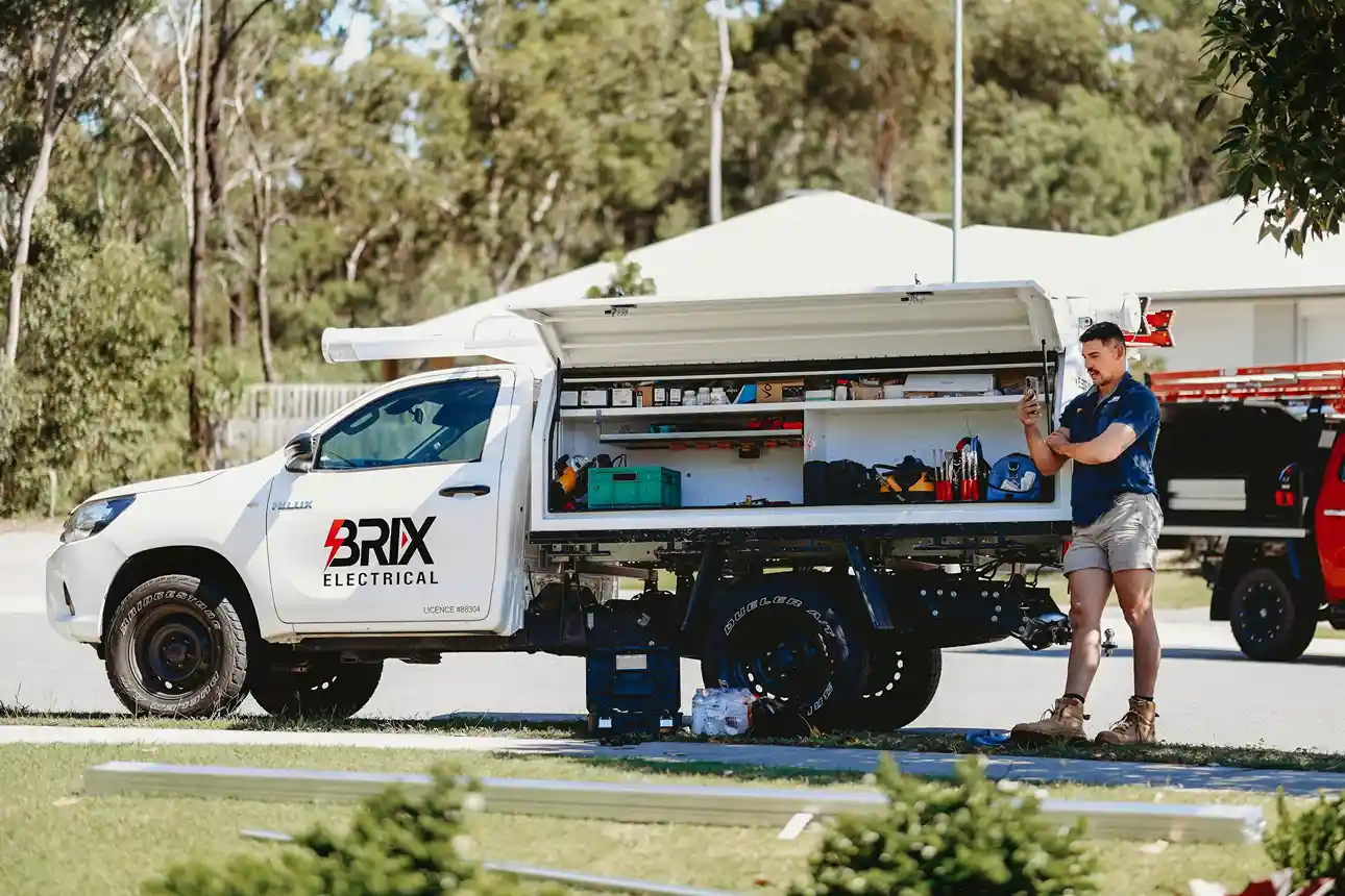 Electrician standing beside a service vehicle organising tools, mobile electrician setup.