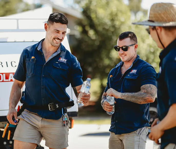 Three electricians in uniform drinking water during a job break, team hydration.