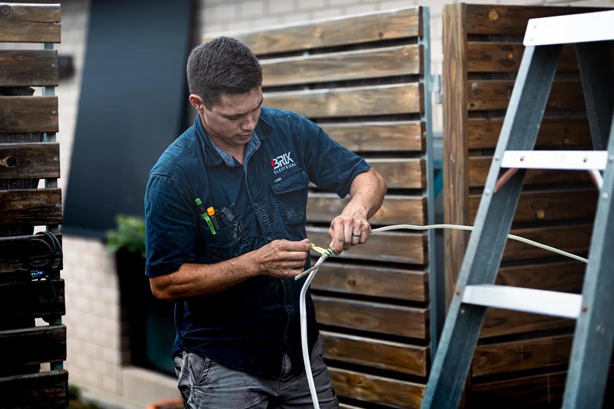 Electrician stripping and connecting electrical wiring outdoors, cable preparation service.