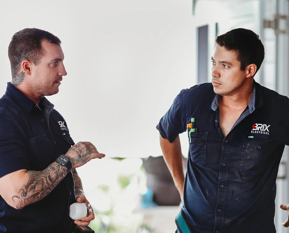 Two electricians discussing work details indoors, showing on-site discussion.