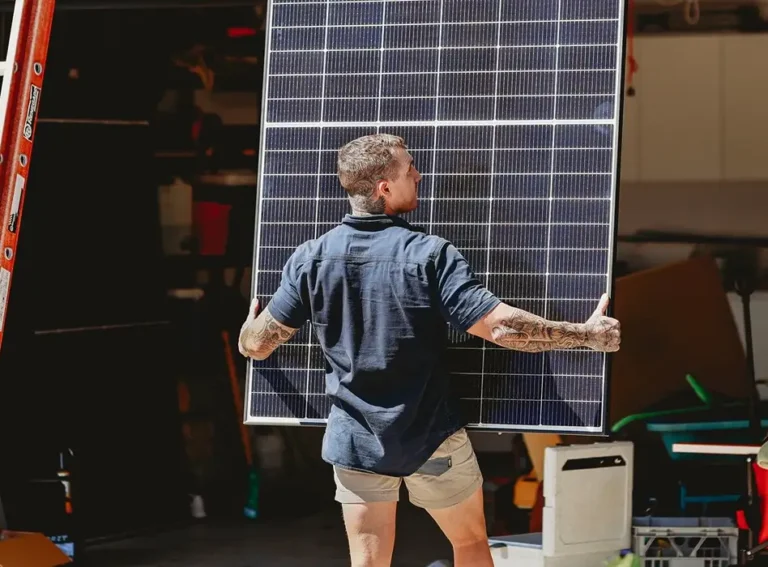 Electrician carrying a large solar panel for installation, showing panel handling work.