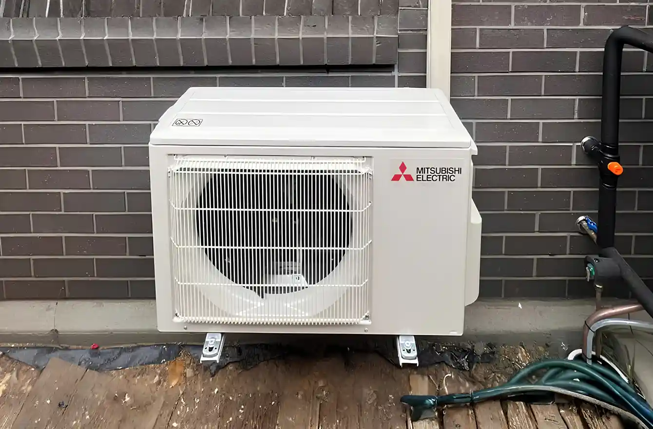 Air conditioning outdoor unit installed beside a house wall, showing outdoor system setup.