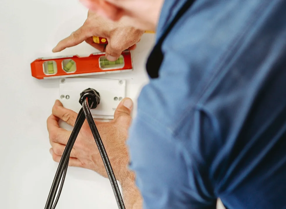 Electrician using a level while installing electrical wiring, showing precise installation work.