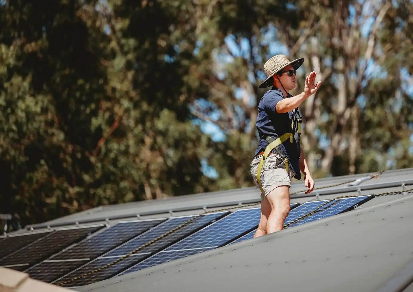Solar installer on roof wearing safety harness near solar panels during installation.