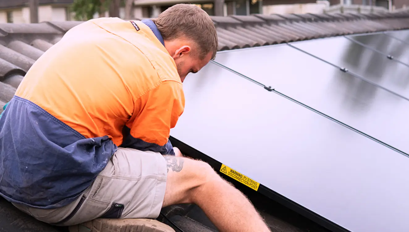Solar installer working on tiled roof connecting and securing solar panel system.