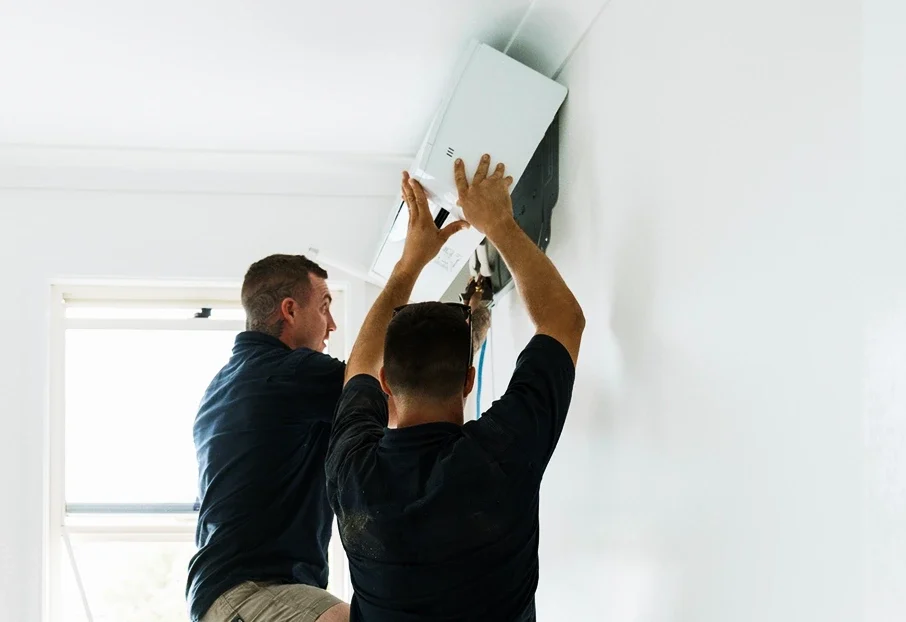 Two technicians installing a wall-mounted air conditioning unit, split system installation.