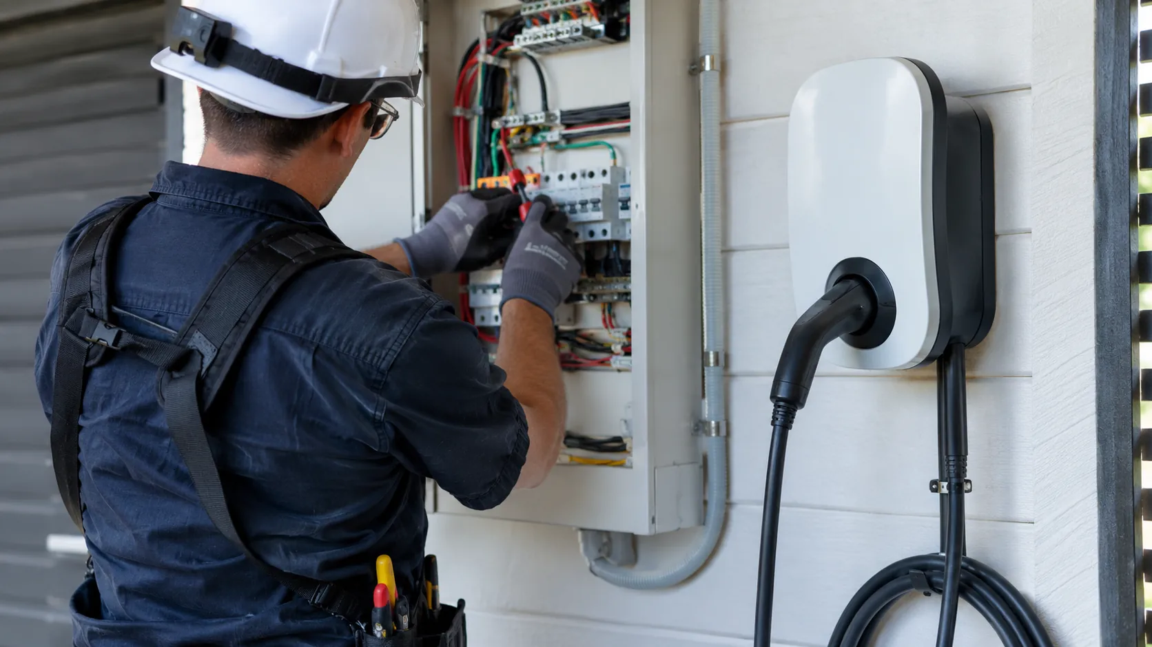 Electrician checking a residential switchboard beside a home EV charger during installation in Ipswich
